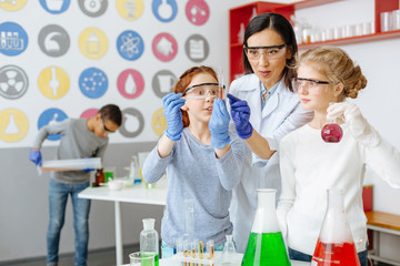 Perfect result. Overjoyed teenage girl pointing at the test tube and showing her teacher and classmate the sediment in it, being excited about the correct result of reaction