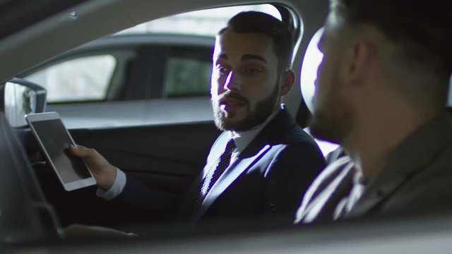 PAN of bearded man sitting in car and talking with auto salesman with tablet