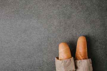 top view of fresh tasty baguettes in paper bags on grey background