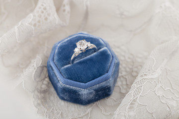 White golden wedding ring with diamonds in blue vintage velvet ring box on gray lace background