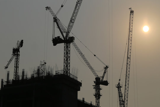 Large construction cranes are building high-rise buildings in the evening.