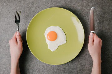 cropped shot of person holding fork and knife ready to eat tasty fried egg on plate