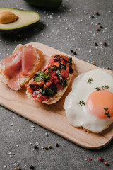 close-up view of delicious antipasto bruschetta and fried egg on wooden cutting board