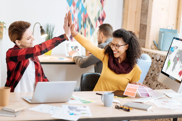 Well done. Good-looking inspired young smart women smiling and giving a high-five while working in...