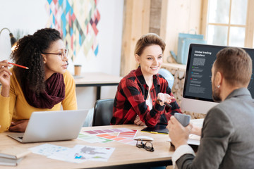 Our team project. Beautiful exuberant blond employer smiling talking with her boss while sitting at the table with her colleague