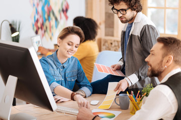 Working together. Good-looking cheerful blond woman smiling and discussing work with her co-workers while sitting at the table