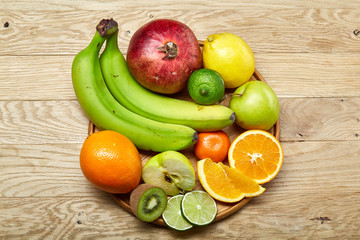 Ripe fresh fruits in a wooden plate on a light wooden background, selective focus, close-up, top view