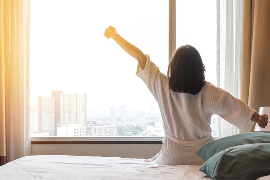Easy lifestyle Asian woman waking up in the morning taking some rest relaxing in hotel room for world lazy day concept