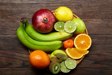 Ripe fresh fruits in a wooden plate on a light wooden background, selective focus, close-up, top view
