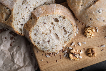 Loaves of gray bread with seeds, in a paper bag, lie on a black table made of wood.