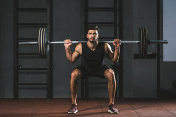 Obraz na płótnie Canvas Young bodybuilder doing exercise with barbell on shoulders in gym