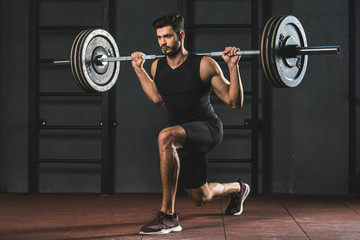 Young sportsman doing exercise with barbell on shoulders in gym