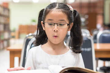 School education and literacy concept with Asian girl kid student learning and reading book in library or classroom