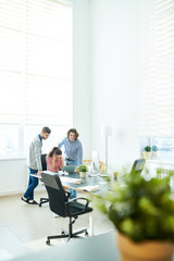 Upset puzzled young Hispanic businesswoman holding head with hands while worrying about failure, her hipster colleagues trying to find solution in office