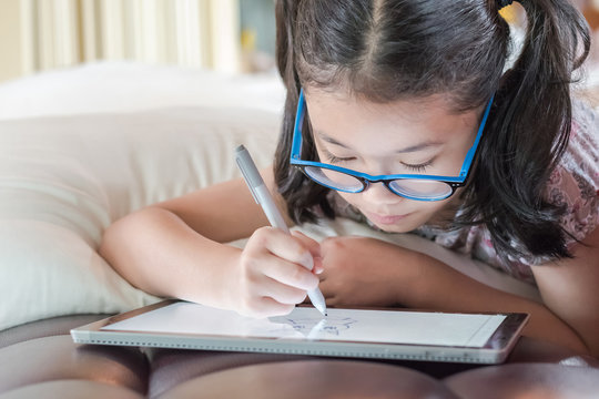 Asian School Child Girl Using Smart  Tablet Device Digital Technology Drawing On Innovative Touchscreen Surface