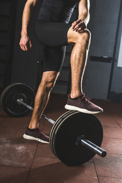 Cropped image of resting sportsman standing on barbell  in gym