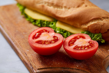 Fresh and tasty sandwich with cheese and vegetables on cutting board over white textured background, selective focus.