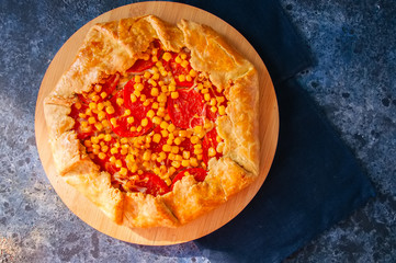 Tomato and sweet corn galette on a wooden board. Top view. Blue stone background.