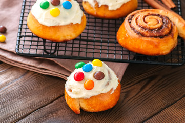 Classic cinnamon rolls - cinnabons with cream cheese frosting with smarties. Wooden background.