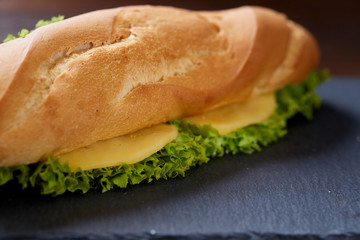 Fresh and tasty sandwich with cheese and vegetables on cutting board over wooden background, selective focus.
