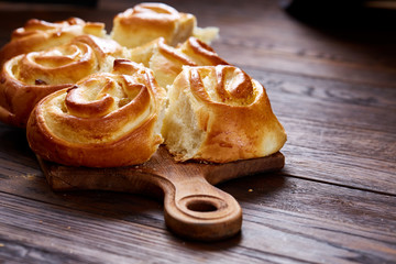 Homemade rose buns on wooden cutting board over rustic vintage background, close-up, shallow depth of field