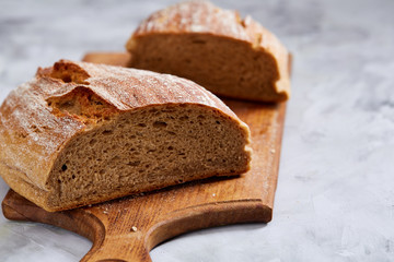 Fresh rye bread loaf on a wooden chopping board over white textured background, shallow depth of field
