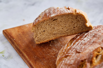 Fresh rye bread loaf on a wooden chopping board over white textured background, shallow depth of field