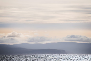 A gentle view of the ocean line and the silhouettes of the mountains in the haze in soft light. Lines of landscape minimalism, simplicity of nature lines. ICELAND
