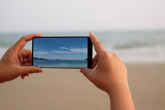 A woman holding a smartphone taking a photo of the sea