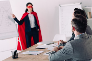 super businesswoman in mask and cape showing presentation for businessman in office