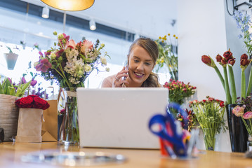 Female florist using laptop at counter in flower shop. Small flower shop owner working on laptop in her shop.