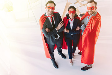 high angle view of super businesspeople in masks and capes with crossed arms looking at camera in...