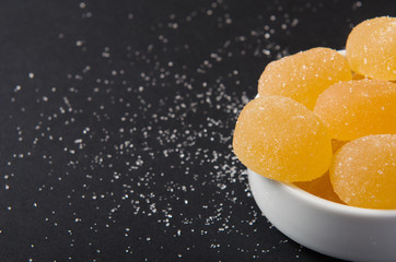Fototapeta na wymiar Marmalade. Yellow, orange candy, sprinkled with sugar in a white bowl on a black background. Copy space