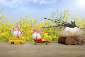 Jaja Wielkanocne na samochodach na tle błękitnego nieba i żółtych kwiatów w promieniach słońca. - obrazy, fototapety, plakaty
