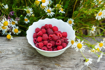 Raspberry on the table with flowers on a wooden table.