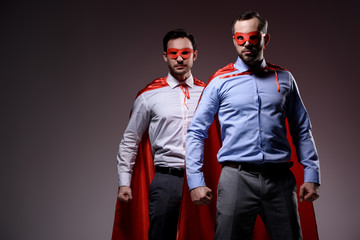 handsome super businessmen in masks and capes standing with fists isolated on grey