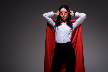 attractive super businesswoman in red cape tying mask isolated on black