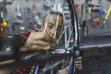 Obraz na płótnie Canvas Mechanic repairing gears of bicycle. Repair and tuning, adjustment, disc brake on a bicycle. Stylish bicycle mechanic woman doing his professional work in workshop.
