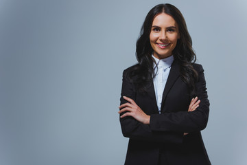 smiling attractive businesswoman standing with crossed arms isolated on grey
