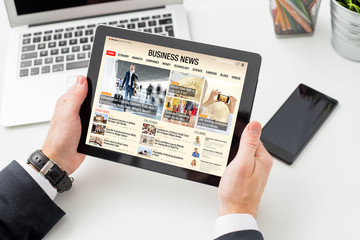 Businessman reading business news on tablet. All contents are made up.
