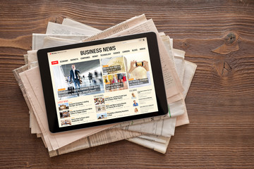 Tablet with business news website on stack of newspapers. All contents are made up.