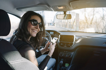 Beautiful young woman using her mobile phone in the car