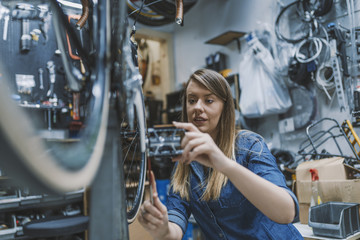 Fototapeta na wymiar Bike service: mechanic servicewoman repairman installing assembling or adjusting bicycle gear on wheel in workshop