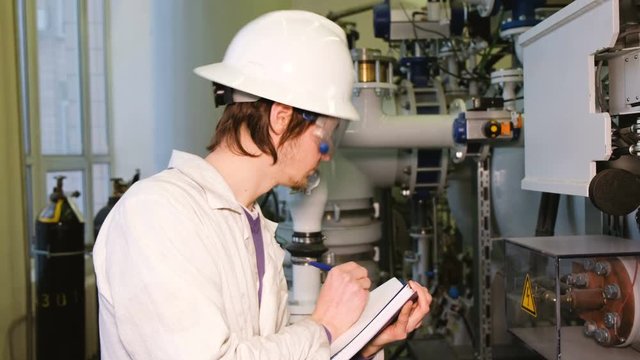 The inspector in a white coat and helmet checks the state of the gas installation in the production laboratory.