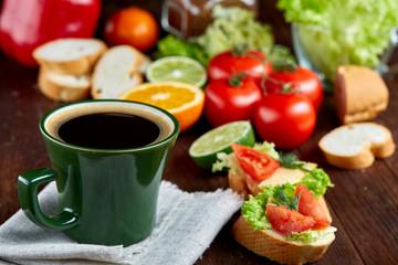 Fresh sandwich with lettuce, tomatoes, cheese on wooden plate, cup of coffee on wooden background, selective focus