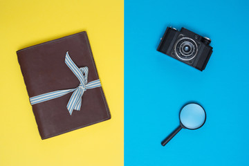 Old notebook, camera and magnifying glass lie on the yellow-blue surface. Vintage style. The play of colors
