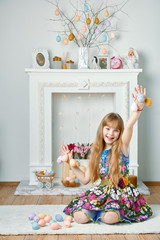 Girl in dress showing knit eggs in risen hands and sitting on carpet on fake fireplace background
