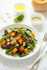 Fresh autumn salad with marinated pumpkin and beetroot, spinach leaves,olive oil, sesame and pumpkin seeds on white table cloth. Space for copy