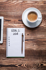 2018 GOALS on his notebook. New year resolutions concept. Top view.