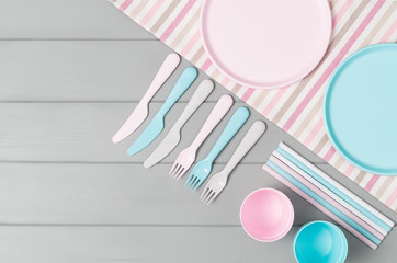 Set of empty, pastel plastic tableware bowls, spoons, knifes and forks isolated on gray wooden background. Flat lay, top view with minimal style.